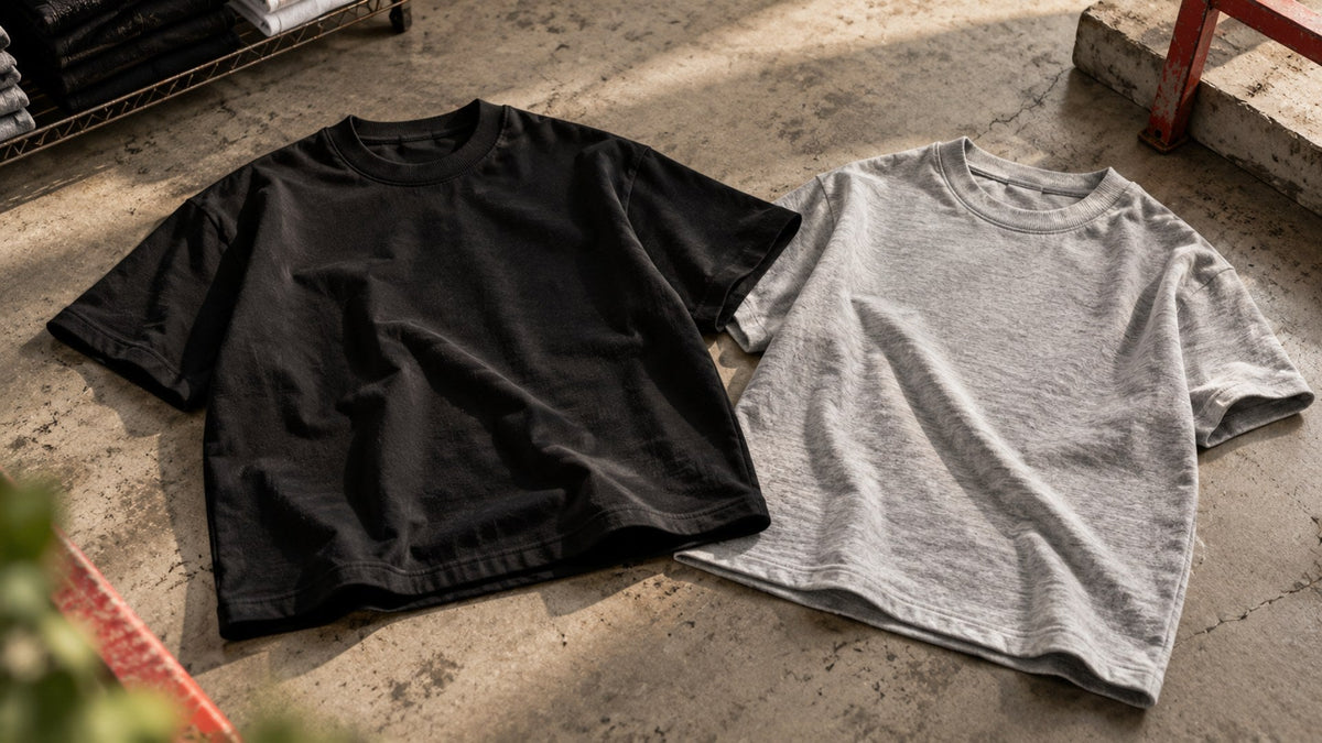 Two heavyweight blank t-shirts, black boxy cut and heather grey classic cut, on concrete